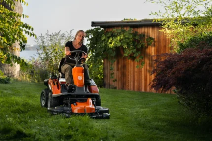 Eine Person, die mit einem Rider-Rasenmäher in einer Gartenumgebung den Rasen mäht.