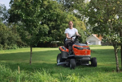 Eine Person, die mit einem Rider-Rasenmäher in einer Gartenumgebung den Rasen mäht.
