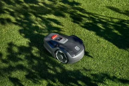 Mähroboter, der auf einem gepflegten Rasen mit Schatten der Bäume arbeitet.