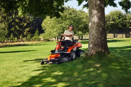 Eine Person, die mit einem Aufsitzmäher in der Nähe eines Baumes in einem Garten Rasen mäht.