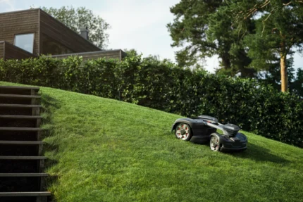 Mähroboter, der auf einem grasbewachsenen Hang in der Nähe eines modernen Hauses betrieben wird.