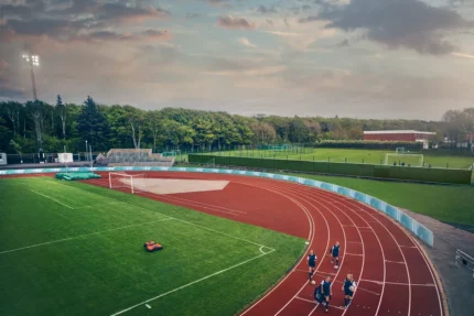 Ein Mähroboter, der auf einem Fußballfeld in der Nähe einer Laufbahn mit joggenden Menschen arbeitet.