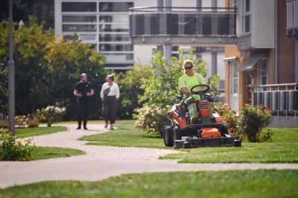 Eine Person, die mit einem Rider-Rasenmäher in einem Wohngarten den Rasen mäht.