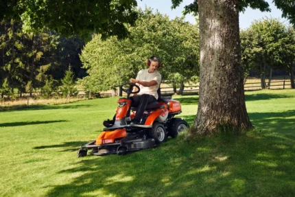 Eine Person, die einen Aufsitzrasenmäher unter einem großen Baum in einem Garten bedient.