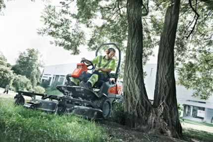 Eine Person, die einen Aufsitzmäher in der Nähe von Bäumen in einem Landschaftsbereich bedient.