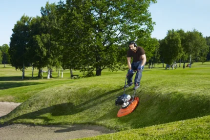 Eine Person, die einen Luftkissenrasenmäher verwendet, um Gras an einer Steigung in einer Parkumgebung zu trimmen.