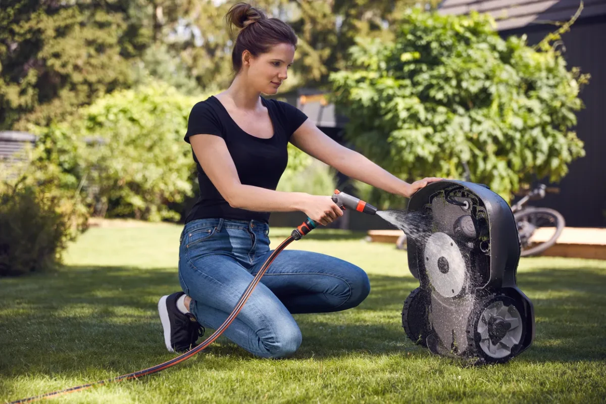 Eine Person, die einen Mähroboter in einem Hinterhof mit einem Gartenschlauch reinigt.