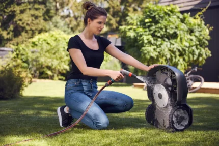 Eine Person, die einen Mähroboter in einem Hinterhof mit einem Gartenschlauch reinigt.