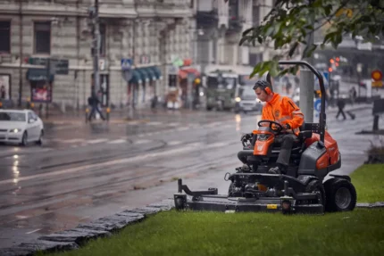 Eine Person, die einen Aufsitzmäher auf einer Rasenfläche neben einer Straße bedient.