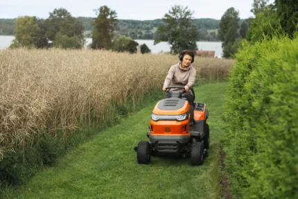Eine Person, die mit einem Rider-Rasenmäher in einem Garten in der Nähe eines Sees einen Rasen mäht.