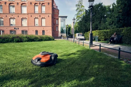 Mähroboter auf gepflegtem Rasen vor einem historischen Backsteingebäude.
