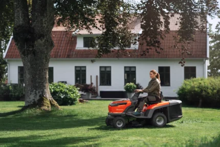 Eine Person, die mit einem Rider-Rasenmäher in einer Gartenumgebung einen Rasen mäht.