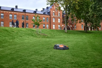 Mähroboter auf einer Wiese in der Nähe eines Backsteingebäudes.